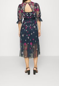 Genomskinlig marinblå klänning med blommig brodyr i rosa, silver och blått. Har en skärning i ryggen och puffärmar. Bärs med svart blockklack sandaler.