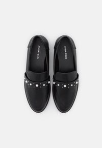 Black leather loafers with a rounded toe and a wide band featuring white pearls and silver accents. Logo visible on the insole.