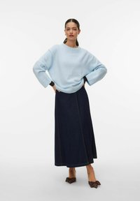 Pull ample bleu clair avec détails côtel és, associé à une jupe maxi en denim foncé avec une couture apparente et des escarpins à pois.