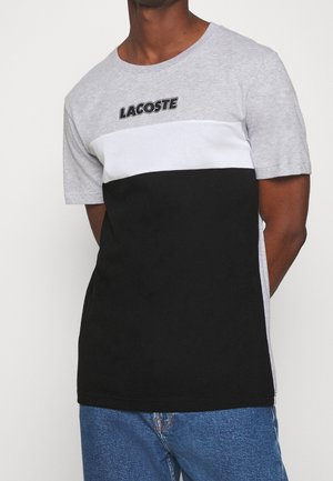 T-shirt à blocs de couleur gris, blanc et noir en coton. Doté d'un col rond, de manches courtes, et du logo Lacoste en travers de la poitrine.