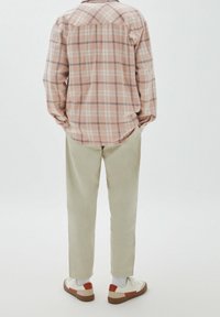 Camisa de franela a cuadros en color rosa claro con mangas largas, combinada con pantalones beiges y zapatillas blancas con acentos rojos y suelas marrones.