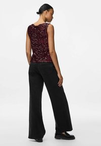 Débardeur en sequins bordeaux avec un col rond, associé à un jean large et noir, vue de dos.