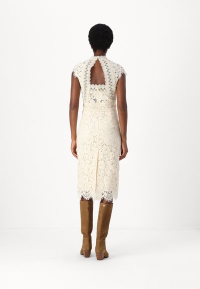 Robe midi en dentelle crème avec un dos plongeant, des manches courtes et des motifs florauxintriqués. Portée avec des bottes au genou en daim marron.