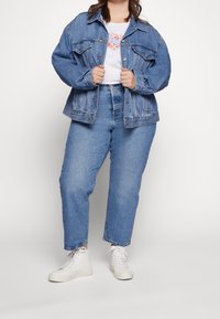 Chaqueta de mezclilla azul clara con un corte relajado, combinada con jeans de tiro alto azul claro y zapatillas altas blancas. Camiseta blanca sencilla por debajo.