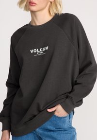 Donkergrijze oversized sweatshirt met een ronde hals, geribbelde boorden en "VOLCOM STONE" in het wit gedrukt op de borst. Casual fit.