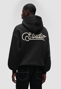 Czarna, oversize bluza z kapturem z dużym kremowym haftem "Studio" na plecach, z kapturem na sznurki i teksturowanym materiałem.