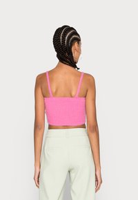 Top de malha cropped rosa com alças finas, apresentando uma textura canelada. Combinado com calças verdes claras de cintura alta.