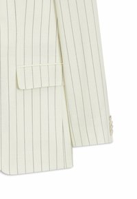 Blazer blanc avec fines rayures verticales noires, poche à rabat et trois boutons sur le poignet de la manche.
