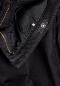 Musta takki, jossa on sileä kangasvuori, kultainen vetoketju, nappikiinnitys ja hienovaraiset tikkausominaisuudet.