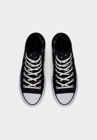 Μαύρα ψηλά αθλητικά παπούτσια με λευκά κορδόνια και σόλες, διακοσμημένα με μικρά κίτρινα αστέρια, σε άποψη από πάνω σε λευκό φόντο.