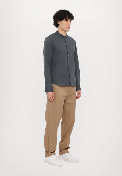Graues Hemd mit Stehkragen, langen Ärmeln, kombiniert mit beigen Hosen und weißen Sneakern. Einfaches Design, lässige Passform.