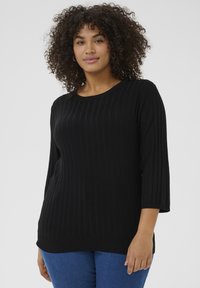 Suéter negro de canalé con cuello redondo y mangas 3/4, con una textura suave y un corte holgado, combinado con jeans de mezclilla azul.
