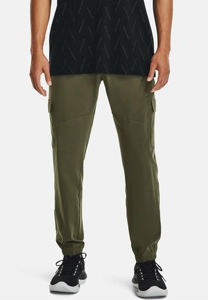 Grüne Cargo-Hosen mit elastischen Bündchen, Seitentaschen und einer glatten, leichten Textur. Kombiniert mit einem schwarzen Grafik-T-Shirt und Sneakers.