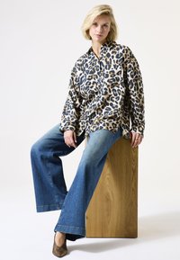 Luipaardprint, knoopshirt in beige, zwart en bruin; wijde blauwe denim jeans; gestructureerde bruine hakken; eenvoudige houten voetstuk.