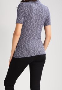 Kortärmad, figursydd topp i ett strukturerat mörkblått och vitt tyg. Har en rund halsringning och en slät yta. Kombineras med svarta byxor.