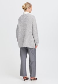 Maglione oversize grigio chiaro con una texture morbida, caratterizzato da un collo alto e spalle abbassate. Abbinato a pantaloni a righe grigi e tacchi bassi.