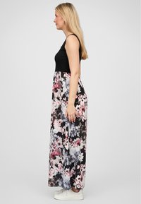 Robe maxi avec un haut noir et une jupe à imprimé floral en rose, violet et blanc. Présente une coupe décontractée et un tissu délicat, assortie à des baskets blanches.