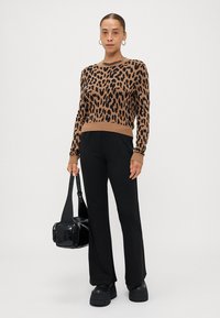 Leopardprint trui in bruin en zwart, met geribbelde manchetten en onderrand, gecombineerd met zwarte wijde broek en een kleine zwarte schoudertas.
