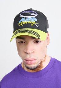 Svart baseballcap med grønn skygge, med brodert "AWGR Racing" logo i blått og gult. Teksturet stoff, buet skygge, justerbar reim.