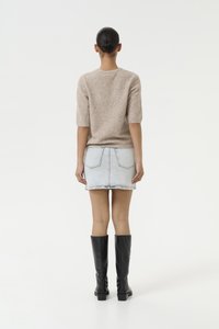 Beige pletený svetr s krátkým rukávem, spárovaný s lehkou džínovou sukní a černými kozačkami po kolena. Hladká textura a ležérní design.