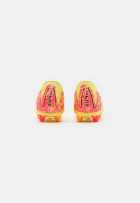Botas de fútbol con un diseño amarillo y rosa. La parte superior de malla presenta un patrón texturizado, y la suela tiene clavos naranjas y rosas para tracción.