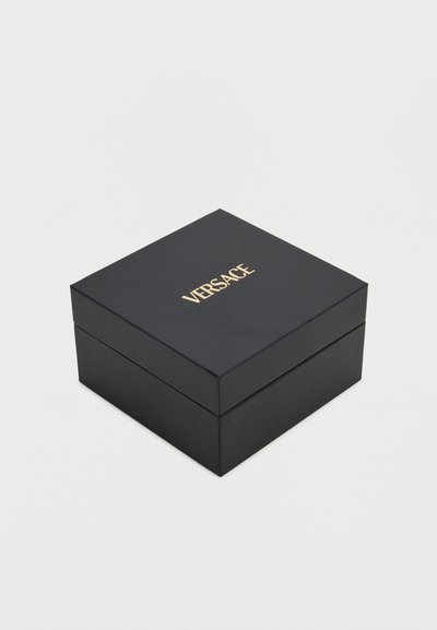 Μαύρο τετράγωνο κουτί με χρυσό λογότυπο "VERSACE" στο κέντρο του καπακιού, πάνω σε λευκό απλό φόντο.