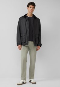 Czarna, lekka kurtka z ostrym kołnierzem, zapinana na guziki z dwoma przednimi kieszeniami, zestawiona z jasnografitowymi spodniami i białymi trampkami.