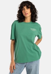 Camiseta de algodón verde con mangas cortas, escote redondo y un logo impreso en el delantero. Corte relajado con una textura suave.