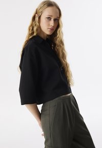 Czarny krótki top z kołnierzykiem i detalami z guzikami, połączony z oliwkowymi spodniami o wysokim stanie, z plisami i bocznymi kieszeniami.