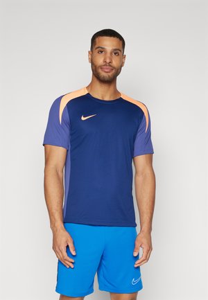 Maglietta sportiva da uomo Nike con torso blu, dettagli arancioni sulle spalle e maniche corte. Abbinata a pantaloni corti blu. Tessuto dalla consistenza liscia.