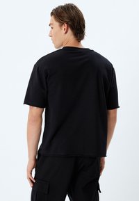 Camiseta negra de manga corta con un corte relajado y dobladillo sin terminar. Confeccionada en tela suave, presenta un cuello redondo y un diseño con mínimos detalles.