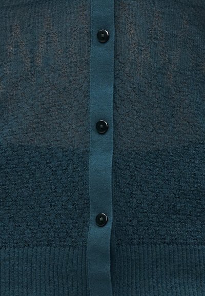 Πλεκτή ζακέτα σε πράσινο-μπλε χρώμα, με υφασμάτινα ανάγλυφα σχέδια, τρία μαύρα κουμπιά και ριμπ τελείωμα, που αναδεικνύει τις διαφορετικές υφές και αποχρώσεις του υφάσματος.