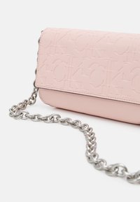 Różowa torebka ze skóry tłoczonej z metalowym łańcuszkowym paskiem na ramię. Charakteryzuje się wyraźnym wzorem z logo, gładką fakturą oraz klapą zamykającą.
