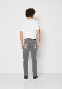 Jeans de mezclilla gris con corte recto, bolsillos traseros detallados y zapatillas negras. La camisa es una simple camiseta blanca de cuello redondo.