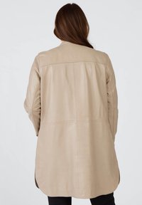 Beige läder långjacka med en slät yta, med rundad fåll och minimala sömdetaljer, designad för en avslappnad passform.