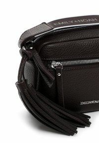 Hnědá texturovaná kožená crossbody taška se zipovým uzávěrem, obsahuje třásně a stříbrné logo na přední straně.