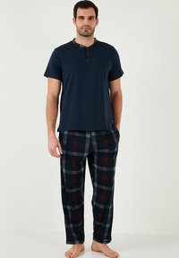 Tricou de pijama din bumbac bleu închis, cu mânecă scurtă și nasturi roșii; pantaloni din flanel cu carouri în nuanțe de bleu închis, roșu și alb. Croială lejeră, textură moale.