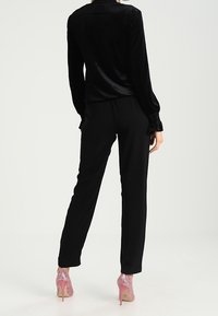 Svart sammet långärmad topp med krage, parat med svarta avsmalnande byxor och rosa glittriga högklackade skor.