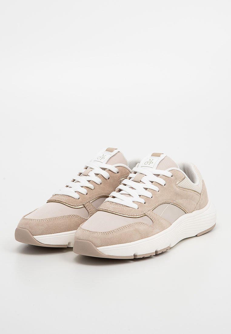 Paar von beigen und weißen lässigen Sneakers mit weißen Schnürsenkeln, strukturierten Sohlen und Logo auf der Zunge, platziert auf einem schlichten weißen Hintergrund.