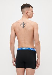 Black boxer briefs with a blue waistband featuring "BJÖRN BORG" text. The fabric appears smooth and stretchy. A tattoo is visible on the back.