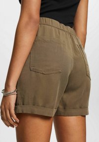 Oliivinvihreät shortsit, jotka on valmistettu sileästä kankaasta. Niissä on joustava vyötärö, käänteet ja kaksi takataskua.