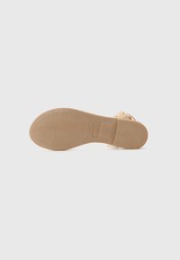 Beige sandaler med flat såle, teksturert gummibunn og justerbar stropp. Designet er minimalistisk med en glatt overflate. Merkevareetikett synlig.