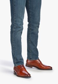 Chaussures habillées en cuir marron avec une texture lisse et un bout arrondi, dotées de lacets bleus et d'un talon bas, assorties à un jean en denim délavé.