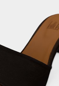 Κοντινή λήψη μαύρου μοκασίνι από σουέτ με ταμπά εσωτερική σόλα από δέρμα και χαμηλό τακούνι σε λευκό φόντο.