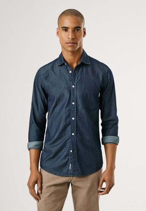 Donkerblauwe denimshirt met een button-down kraag, één borstzak en opgerolde mouwen, met witte knopen en een gladde textuur.