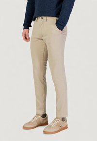 Pantalones ajustados beige con textura suave, que cuentan con bolsillos frontales y cierre de botón. Combinados con zapatillas de deporte de color claro.