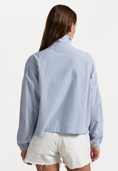 Camisa às riscas azul e branca com colarinho, mangas longas, ombros caídos e bainha curta, combinada com calções brancos desfiados.