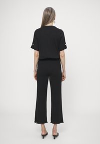 Černý zkrácený top a široké kalhoty z žebrované látky. Obsahuje krátké rukávy s tlačítkovými detaily a nezpracované lemy. Hladká textura, minimalistický design.