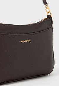 Donkere bruine leren schoudertas met een grofnerf uiterlijk, gouden rits en kettingdetail, met een klein goud "Michael Kors" logo op de voorzak.