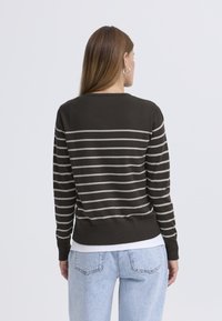 Pull rayé marron avec des lignes grises horizontales, poignets et ourlet côtelés, coupe ajustée. Porté sur un haut blanc, associé à un jean bleu clair.